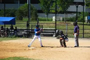 A batter, catcher, and umpire are positioned and ready for a pitch in a sunny baseball game.