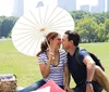 A couple enjoys a sunny picnic in a grassy park with a white parasol and the city skyline in the background