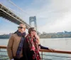 A couple is enjoying a sunny day on a boat cruise with a scenic suspension bridge in the background