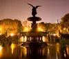 The image captures a beautifully lit angelic statue atop a fountain with water reflections in a serene park at twilight