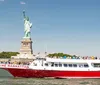 A red and white boat named THE MANHATTAN is filled with passengers near the Statue of Liberty under a clear blue sky