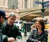 A group of people appears engaged in conversation near the entrance of Grand Central Terminal on a cloudy day with street signs for East 42nd Street and Park Avenue visible above them