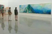 Three individuals are standing in an art gallery, observing a large, colorful abstract painting.
