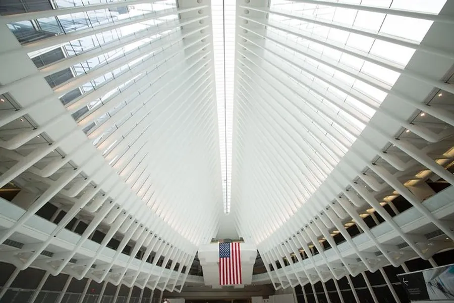 The image shows the interior of a modern building with a white ribbed ceiling structure leading the eye towards a hanging American flag.
