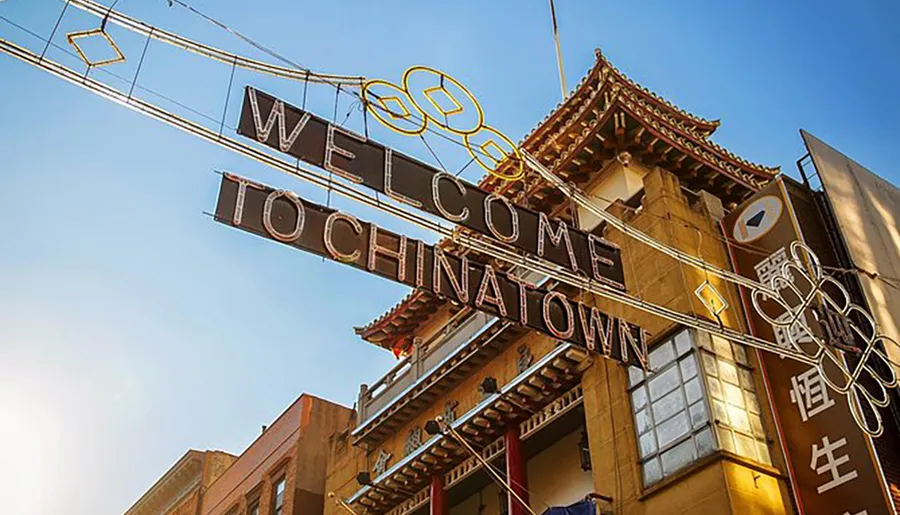 An elaborate gateway with an illuminated Welcome to Chinatown sign and decorative elements in a city setting under a clear sky.