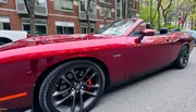A person is sitting inside a red convertible car parked on a tree-lined street.