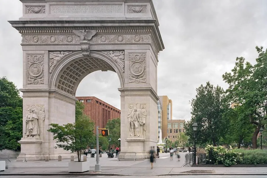 The image shows the Washington Square Arch, an iconic marble triumphal arch in Washington Square Park, New York City, with trees, pedestrians, and buildings in the background.