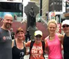 Five people are posing together for a photo in what appears to be Times Square with a statue and the iconic red steps in the background
