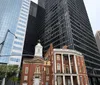 The image shows an old church in the foreground juxtaposed against a backdrop of modern skyscrapers illustrating a contrast between historical and contemporary architecture in an urban setting