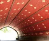 A person is sitting under a curved red-patterned brick underpass or tunnel with daylight showing at the end