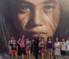 A group of people is standing in front of a large mural that features a hyper-realistic face of a woman showcasing striking details especially in the eyes