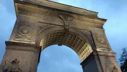 This image shows the intricately detailed Washington Square Arch in New York City, lit by a soft glow against the evening sky.