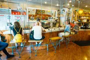 This image shows a group of customers seated on unique swing-like bar stools at a coffee shop counter, while a barista works in the background.