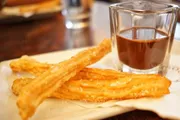 A plate of fresh churros is accompanied by a glass of chocolate sauce for dipping.