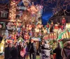 The image captures a vibrant and densely decorated house with festive Christmas lights and ornaments observed by a crowd of people enjoying the holiday display at dusk