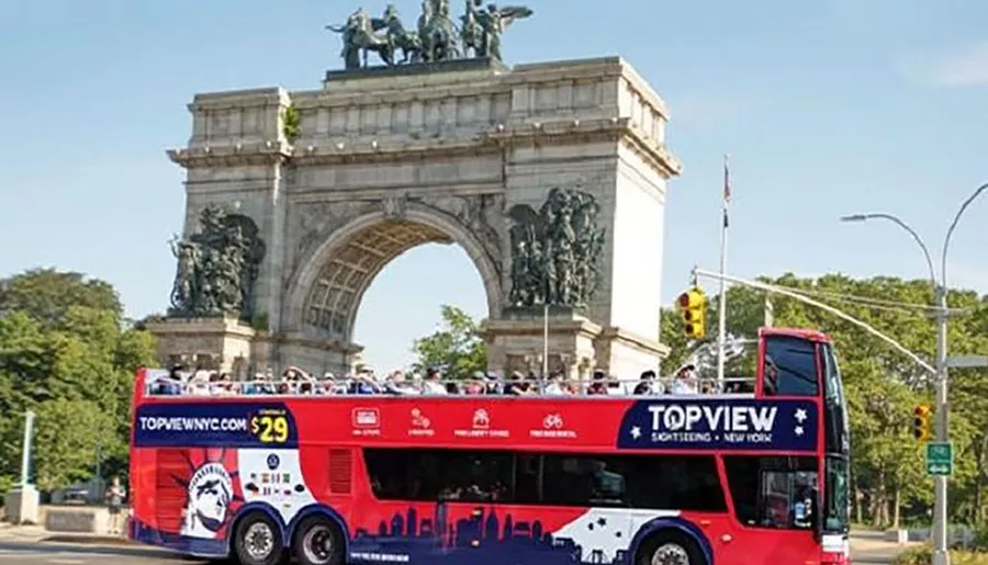 A red double-decker sightseeing bus is passing by a grand arch monument, with tourists on the open-top upper deck enjoying the view.