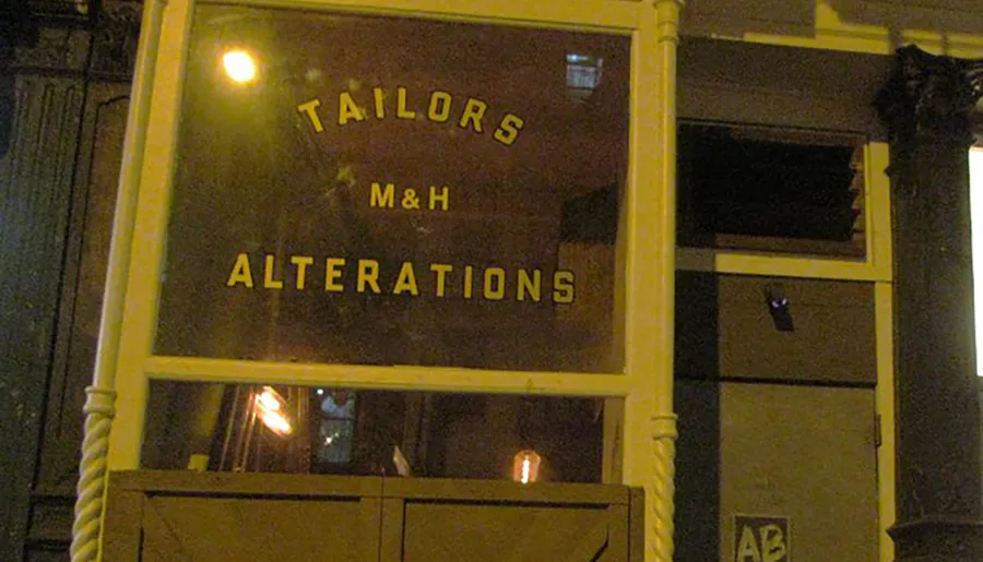 The image is of a storefront at night with a sign that reads TAILORS M&H ALTERATIONS.