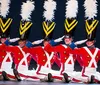 A group of dancers in matching candy cane-inspired costumes perform in a festive setting adorned with large hanging ornaments