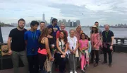 A diverse group of individuals is posing for a group photo with the New York City skyline in the background.