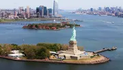 An aerial view of the Statue of Liberty with the New York City skyline in the background and Ellis Island nearby.