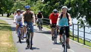 A group of people are enjoying a bike ride along a path by the water on a sunny day.