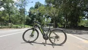 A bicycle is parked in the middle of a paved path in a park with trees and people in the background.