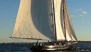 A large sailboat is gliding over the water filled with passengers enjoying a sunny day at sea.
