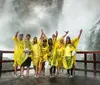 A group of people wearing yellow rain ponchos are cheerfully posing in front of a powerful misty waterfall