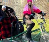 Two passengers are enjoying a rickshaw ride in a park while the cyclist smiles for the camera
