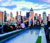 A group of people are enjoying a rooftop gathering during sunset with a view of a city skyline