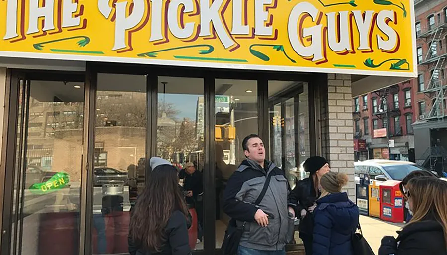 People are standing in front of a store named The Pickle Guys, suggesting a bustling scene possibly indicative of the store's popularity.