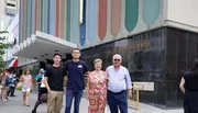 Two younger men and an older couple pose for a photo on a city sidewalk, with the entrance of The Greater Refuge Temple building as their backdrop.