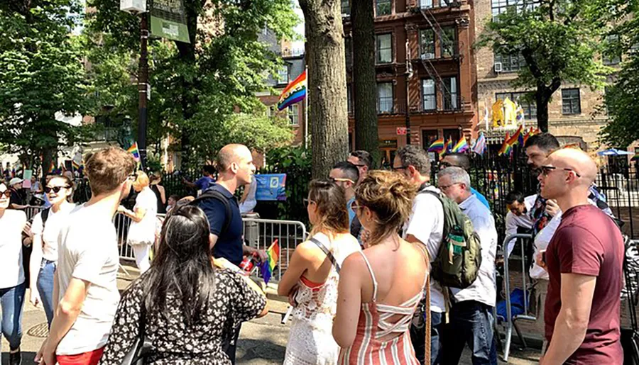 A diverse group of people gather at an outdoor event adorned with rainbow pride flags.
