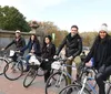 A group of cheerful people on bicycles are posing for a photo waving and smiling in a park-like setting