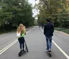 Two people are riding electric scooters along a path with greenery in the background