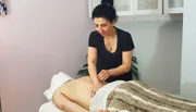 A practitioner is performing a treatment on a patient who is lying down on a therapy table.