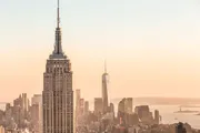 The image features the Empire State Building in the foreground with the skyline of Lower Manhattan in the background, bathed in the warm glow of a sunset.