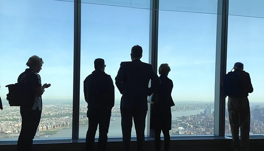 Five silhouetted figures stand before a large window overlooking a cityscape, with the bright daylight casting them in shadow.
