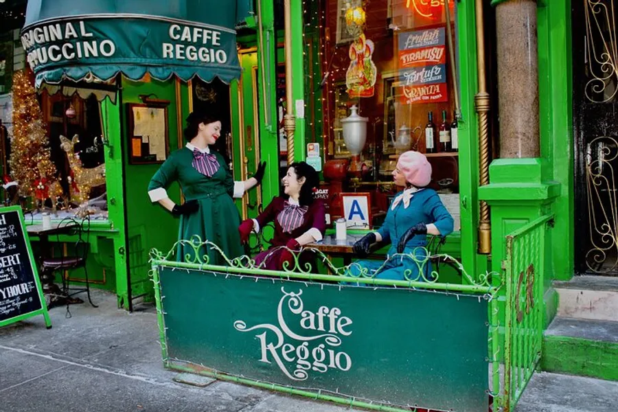 Three individuals are seated and interacting in front of a vibrant green café named Caffè Reggio, adorned with festive decorations and the sign Original Cappuccino.