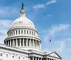 The image shows a close-up view of the United States Capitol dome with the American flag flying nearby against a partly cloudy sky